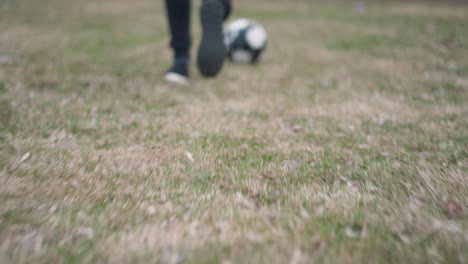 close-up leg view of someone running with a soccer ball on a grassy field, captured just before they shoot the ball away