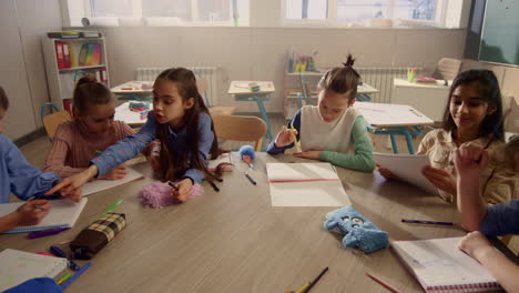 Students-talking-during-lesson-at-round-desk.-Cheerful-kids-having-lesson