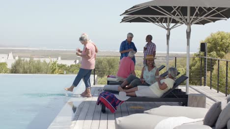 happy diverse senior friends talking and relaxing by pool in sunny garden, unaltered, in slow motion