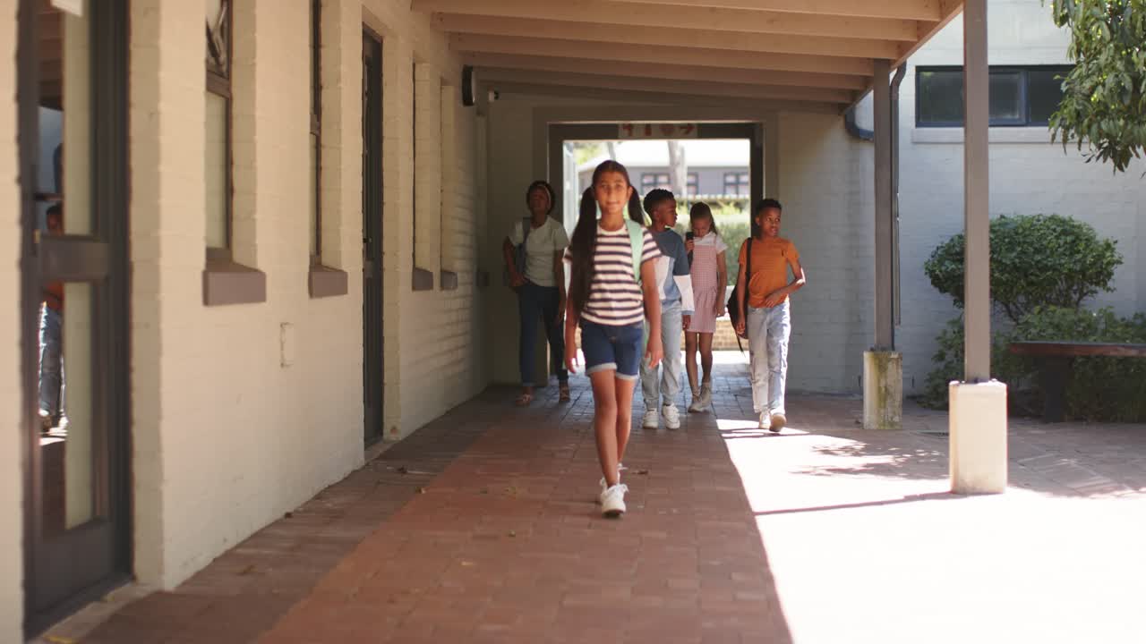 Un gruppo eterogeneo di adolescenti segue un ragazzo afroamericano che sta entrando in un passaggio, mentre cammina per il campus con delle borse