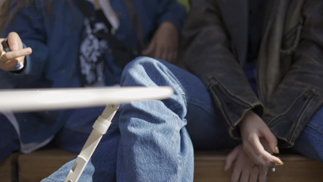 두 명의 알아볼 수 없는 소녀들이 야외에서 휴식을 취하고, 손으로 담배를 피우고 있습니다.