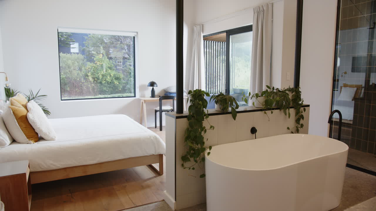 Modern bedroom with freestanding bathtub and lush green plants for relaxation, copy space