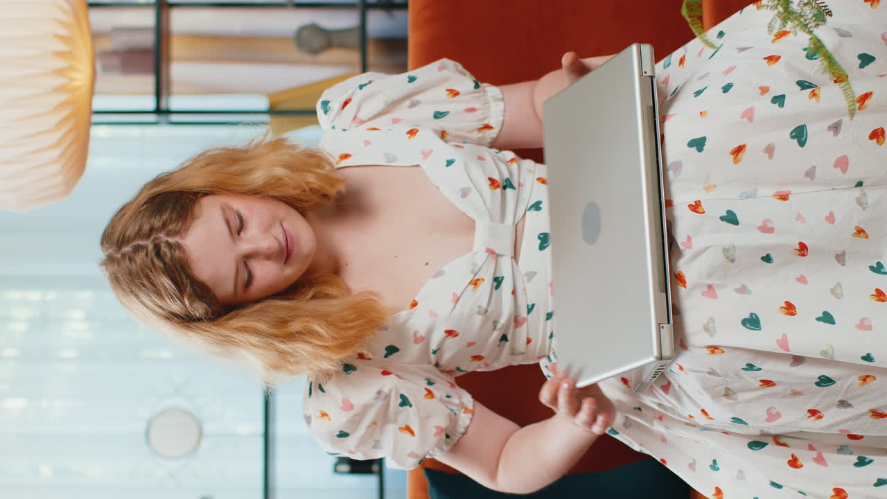 mujer joven independiente sentada en el sofá cerrando la computadora portátil después de terminar el trabajo en la habitación en casa