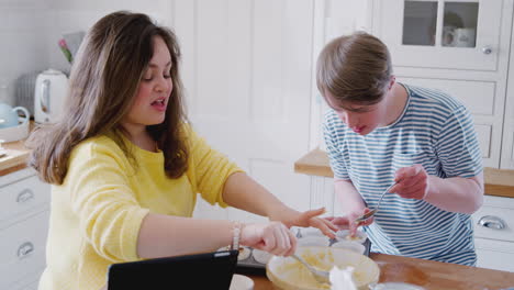 young downs syndrome couple putting mixture into paper cake cases in kitchen at home