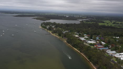 Toma-Aérea-De-Un-Dron-Rastreando-Un-Barco-Que-Avanzaba-Por-El-Río-Shoalhaven-En-Un-Día-Tormentoso-En-La-Costa-Sur-De-Nueva-Gales-Del-Sur,-Australia