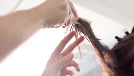 hands of caucasian male hairdresser combing client's long hair at hair salon, slow motion