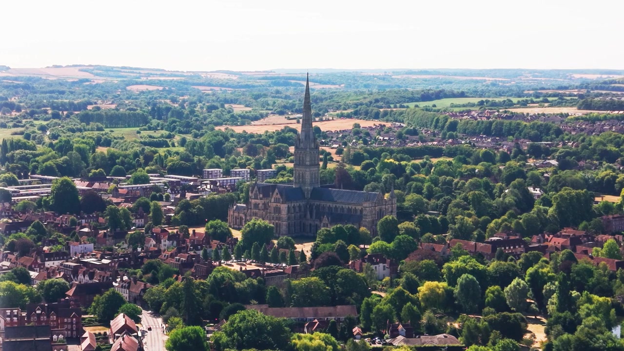 Ampia vista aerea della Cattedrale di Salisbury e della sua famosa guglia che si erge sopra gli alberi, i tetti storici e la campagna del Wiltshire.