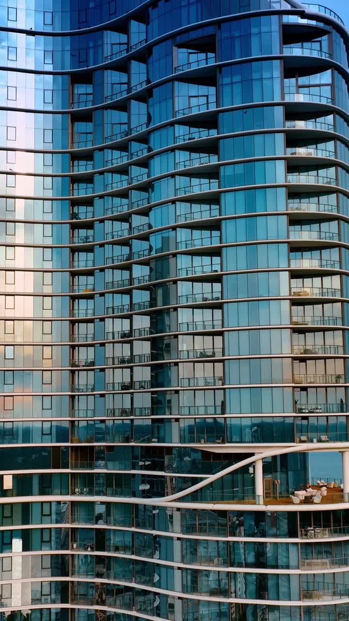 Alejándose de un hermoso y moderno bloque de apartamentos de gran altura con fachada de espejo. Edificio en la orilla del océano en Miami, Florida, EE. UU. Video vertical.