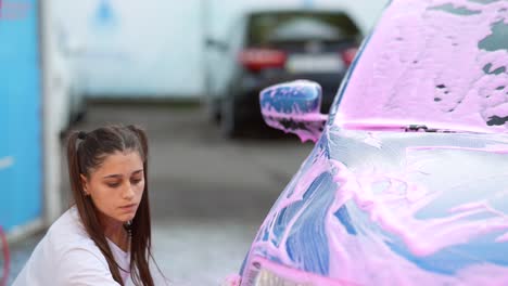 mujer lavando un coche con espuma de jabón rosa