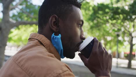 Afroamerikanischer-Geschäftsmann-Mit-Gesichtsmaske,-Der-Im-Park-Kaffee-Trinkt