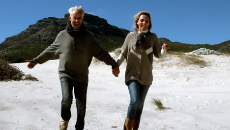 Una-Pareja-Madura-Despreocupada-Corriendo-Tomados-De-La-Mano-En-La-Playa