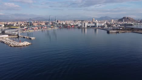 aerial panning view of the industrial port of alicante, with the city and castle in the background