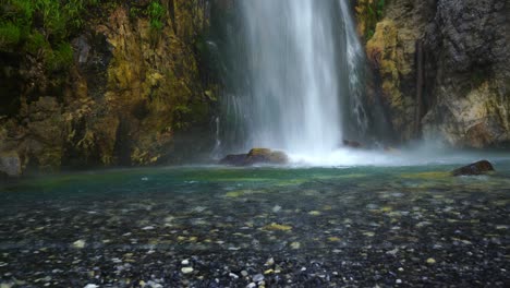 Waterfall-colorful-pond-surrounded-by-cliffs-and-pebbles-in-Theth-mountains,-Albania