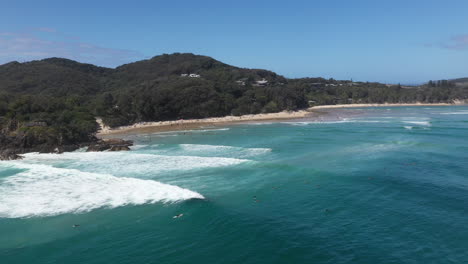 Wide-rotating-drone-shot-of-surfers-in-the-water-and-island-in-background-at-Wategos-Beach,-Byron-Bay,-Australia