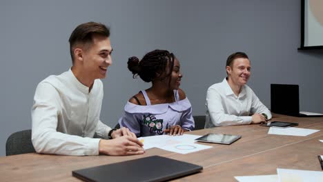 un grupo de gerentes creativos multiétnicos desmonta en la reunión de la junta directiva en la sala de conferencias los gráficos de las ganancias del último año en la empresa. una chica afroamericana y un europeo trabajan en un equipo