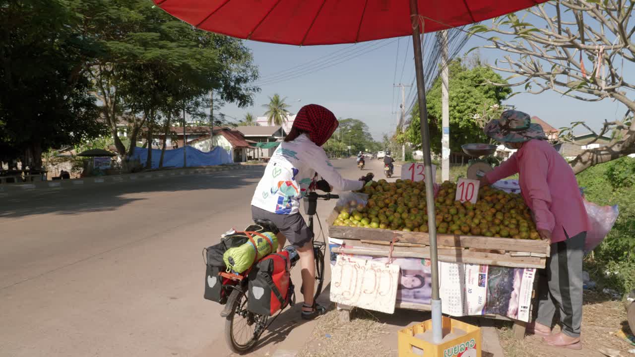 mujer en bicicleta recogiendo fruta fresca del puesto callejero local en el sudeste asiático