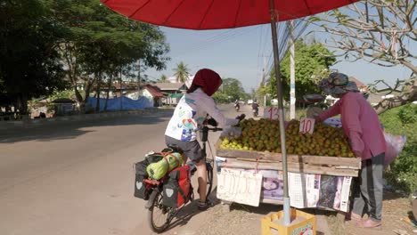 woman on bike picking fresh fruit from local street stall in southeast asia