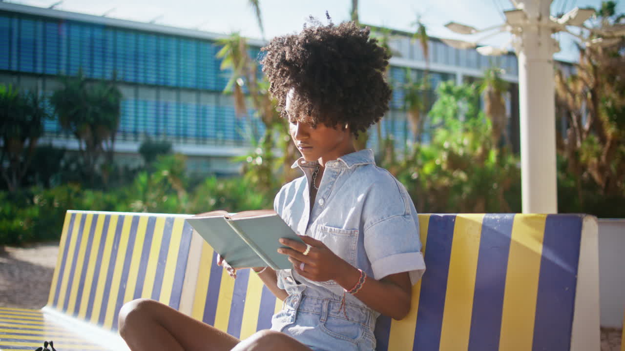 Teen girl studying textbook sitting campus bench close up. Student reading book.
