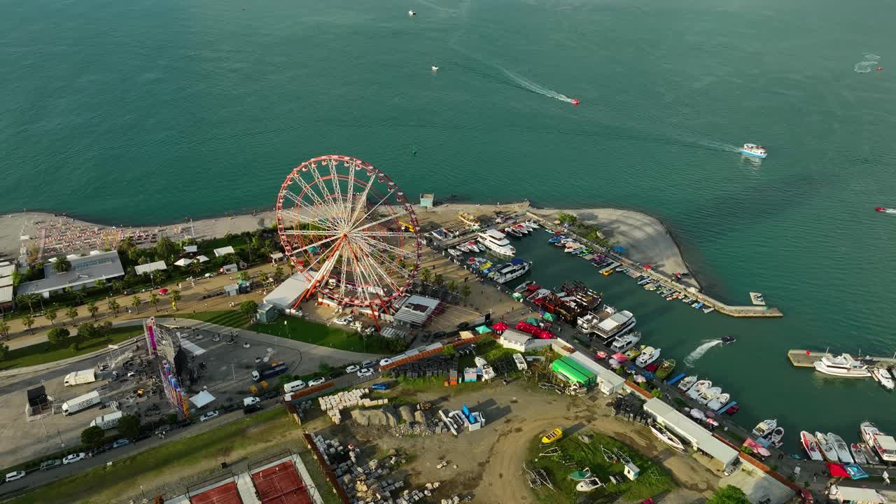 An aerial shot of Batumi’s amusement park located beside the Black Sea, featuring a large Ferris wheel, colorful tents