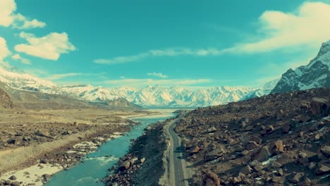 drone is flying slowly over a river in skardu with a view of a high mountain range covered in snow