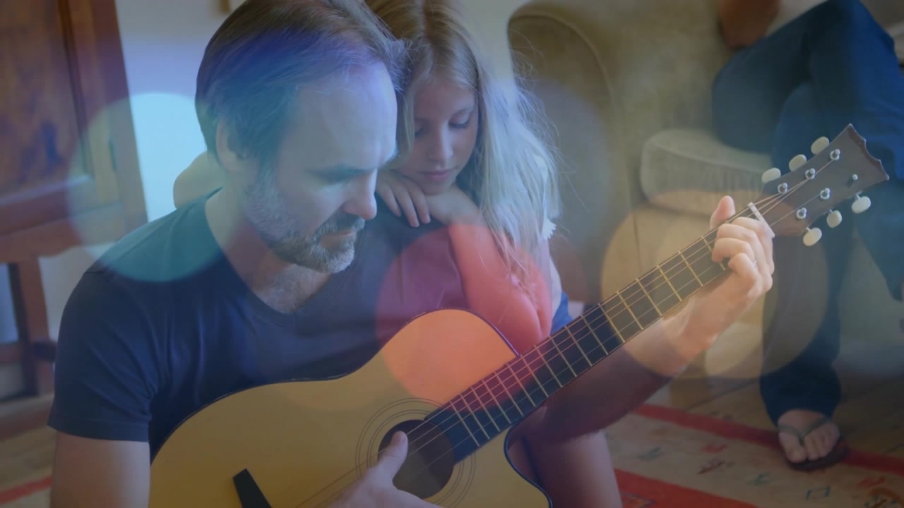 Ojciec grający na gitarze w pokoju, z córką opierającą się na jego ramieniu, podczas gdy matka obserwuje rozbłyski kolorów.