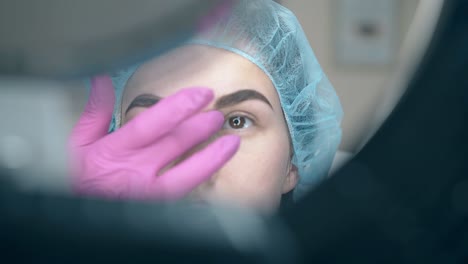 el cosmetólogo pone la regla de la ceja en la cara del cliente con tatuaje
