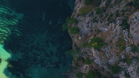 Bird-view-of-pristine-cliff-coast-beach-bay-with-clear-turquoise-water-and-trees-on-Palma-de-Mallorca-Island