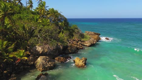 Spectacular-low-flight-above-rocky-tropical-remote-coastline-with-green-shallow-water-and-waves-breaking-on-shore,-Dominican-Republic,-above-aerial-approach