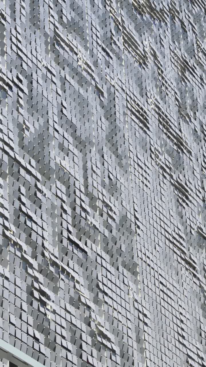 Vertica shot of a textured surface resembling waves or ripples, part of a building situated in Brickell, Miami, glimmers under a clear, sunny sky, adding a modern architectural touch to the area.