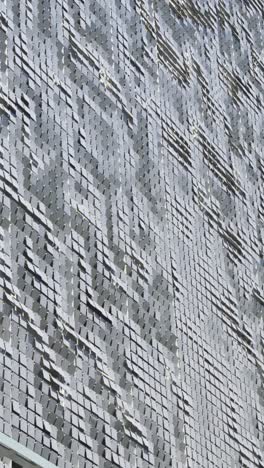 vertica shot of a textured surface resembling waves or ripples, part of a building situated in brickell, miami, glimmers under a clear, sunny sky, adding a modern architectural touch to the area.