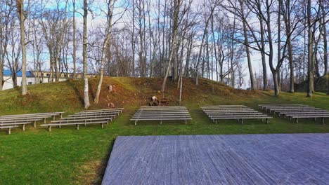 Outdoor-stage-and-benches-in-green-woods,-tracking-drone-shot