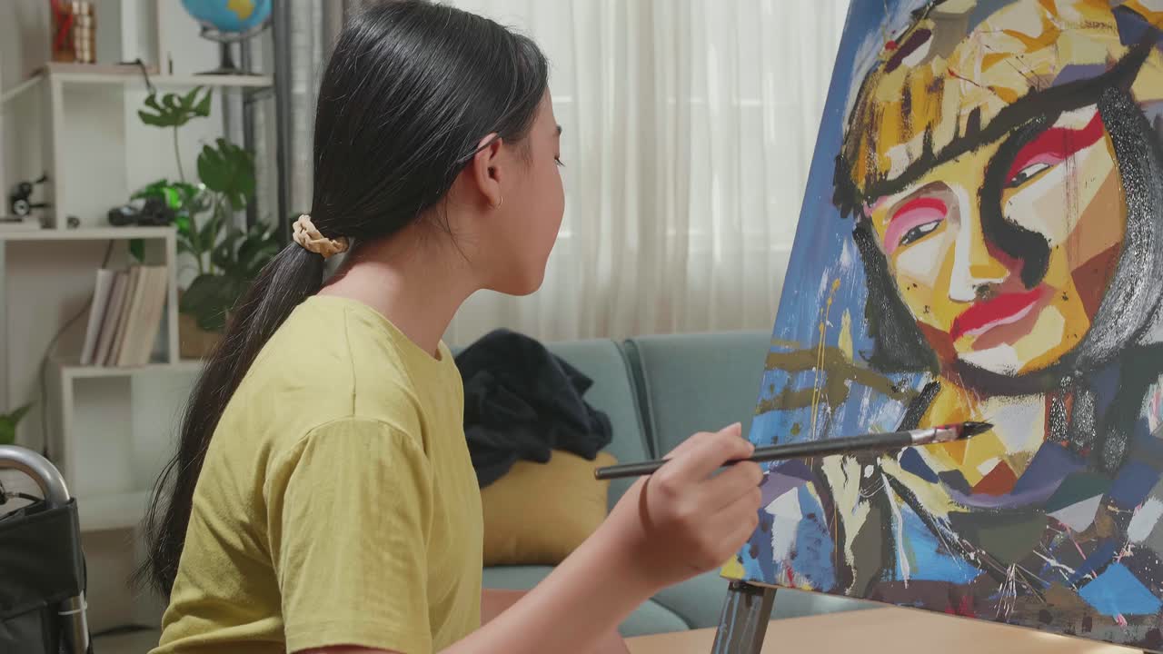 Side View Of An Asian Artist Girl In Wheelchair Holding Paintbrush Mixed Colour Thinking And Painting A Girl On The Canvas
