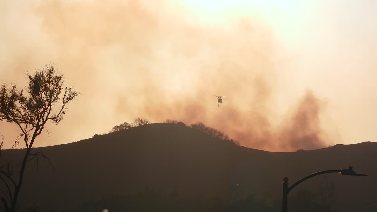 Fire emergency helicopters during the day flying over fire in Los Angeles hills, California, USA, static shot, silhouette