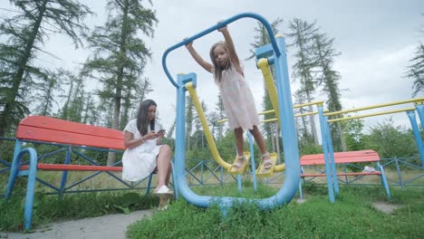 a pregnant mother and her young daughter enjoy playful time together at a playground in the park, surrounded by trees and greenery