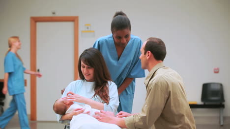 smiling nurse behind a smiling mother and a father with their baby