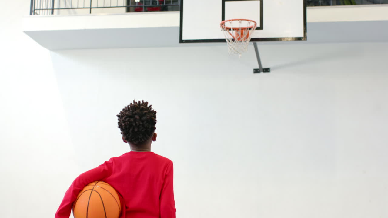 african american boy holding basketball, focusing on hoop in school gym, copy space