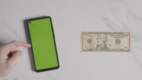 overhead currency shot of us 10 dollar bill next to person using green screen mobile phone