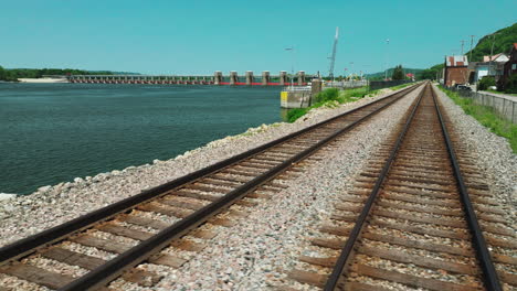 Low-sideways-dolly-shot-of-railway-passing-next-to-lock-and-dam-4,-USA