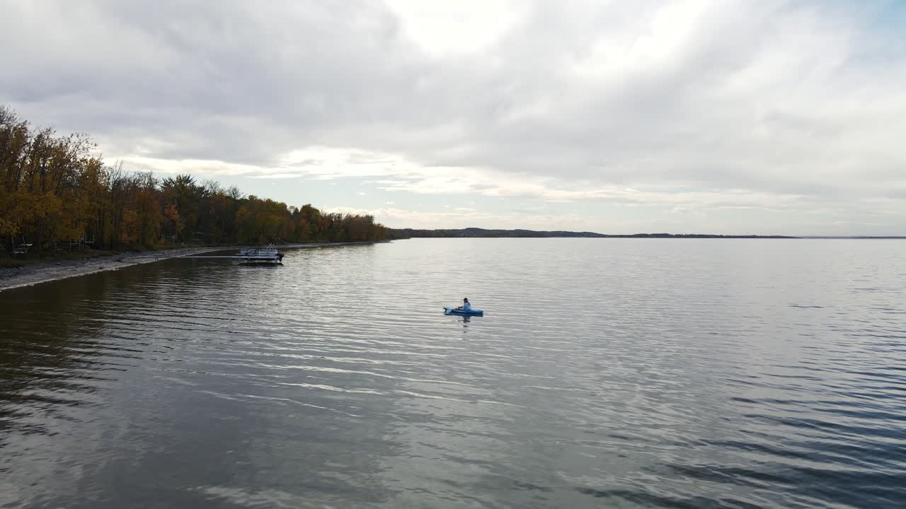 파란색 카약에 앉아 앨버타 주 버팔로 호수의 해안선을 따라 천천히 노를 젓는 사람