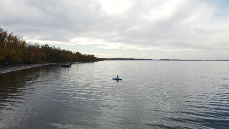 person sitting in a blue kayak, paddling slowly along the shoreline of buffalo lake, alberta