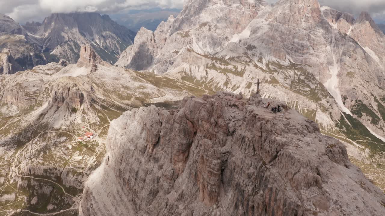 toma aérea sobre la cruz de la cumbre del monte paterno, con rifugio localli en tre cime, dolomitas