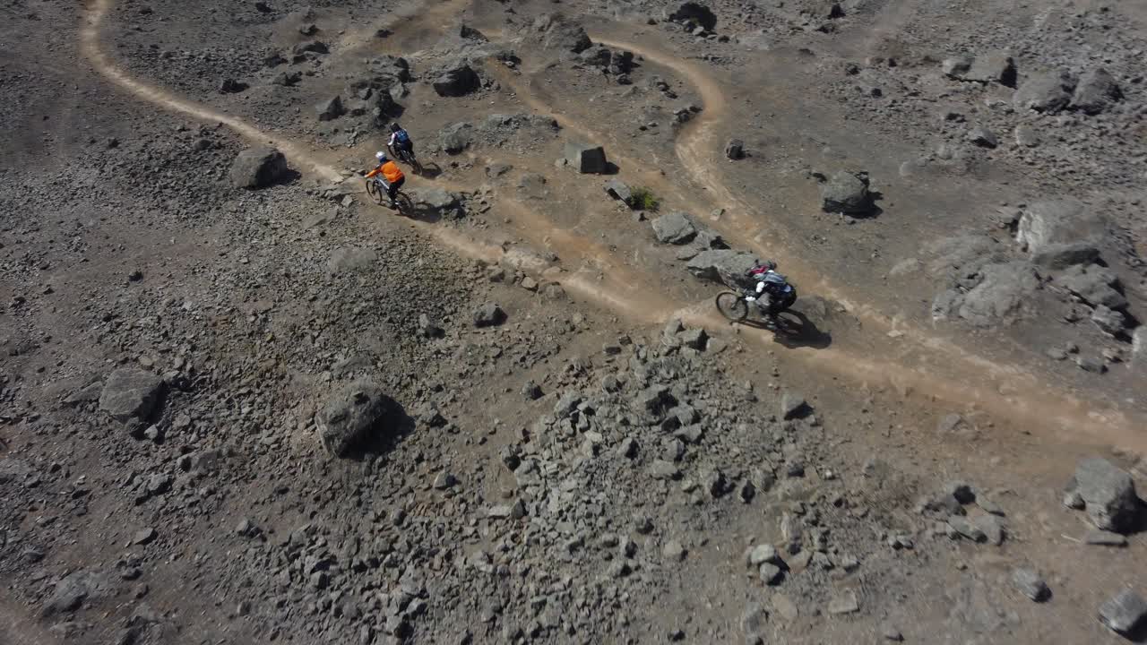 Ripresa dinamica con drone di mountain biker che scendono su piste sterrate su un sentiero di montagna roccioso