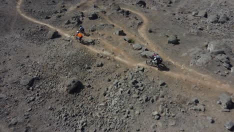 dynamic drone shot of mountain bikers going downhill on dirt tracks on a rocky mountain path