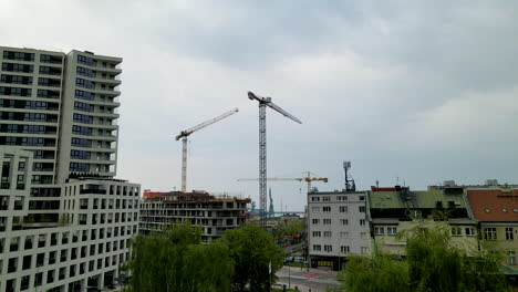 Vista-Aérea-De-Grúas-En-El-Sitio-De-Construcción-En-Una-Zona-Residencial-Polaca-Con-Bloques-Y-Apartamentos-Durante-El-Día-Nublado