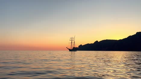 Silhouette-of-ancient-sailing-ship-with-lowered-sails-navigating-at-sunset-seen-from-moving-boat