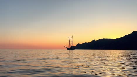 silueta de un antiguo barco de vela con velas bajadas navegando al atardecer visto desde un barco en movimiento