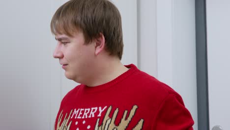 young man in red knitted sweater with print of rudolf the fawn looks at craft paper bag in thought, then opens wardrobe and throws package inside. guy hides christmas present to make surprise.