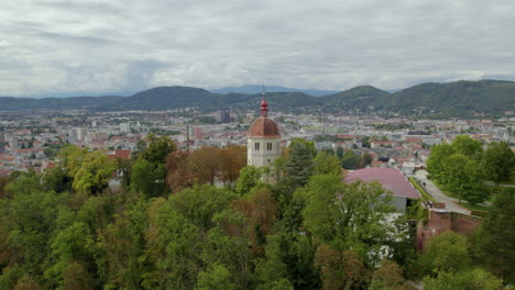 vista aérea volando lejos de la torre glockenturm en el parque arbolado schloßberg hilltop de graz