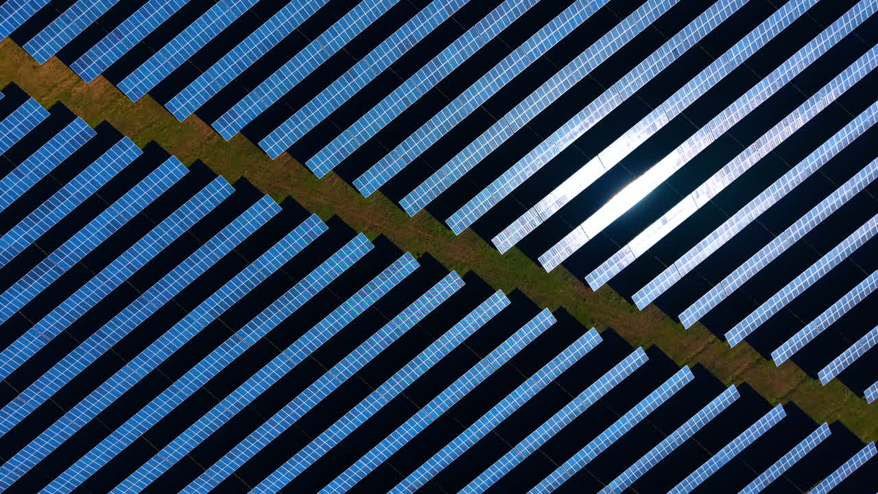 Vista dall'alto di pannelli solari con il riflesso del sole. Motivo aereo geometrico di file fotovoltaiche con un brillante luccichio di luce solare sulla superficie.