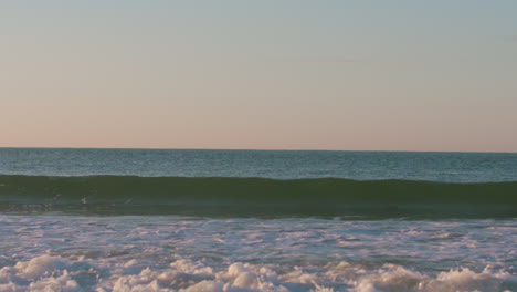 Small-waves-breaking-during-a-calm-sunrise-in-Luz,-Portugal